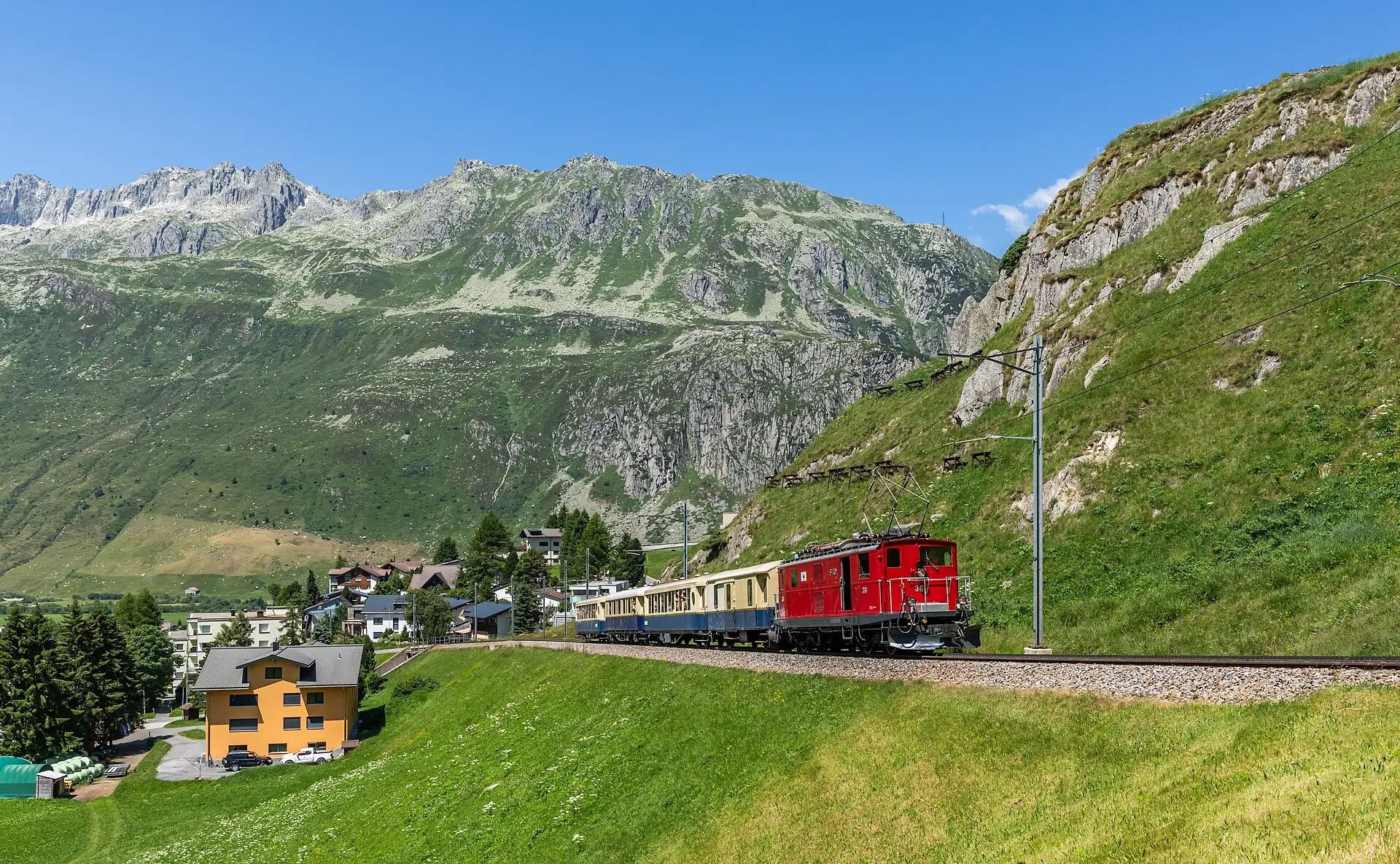 A couple beside the red-and-white lighthouse on the Oberalp Pass, with bare green slopes and Lake Oberalp behind them
