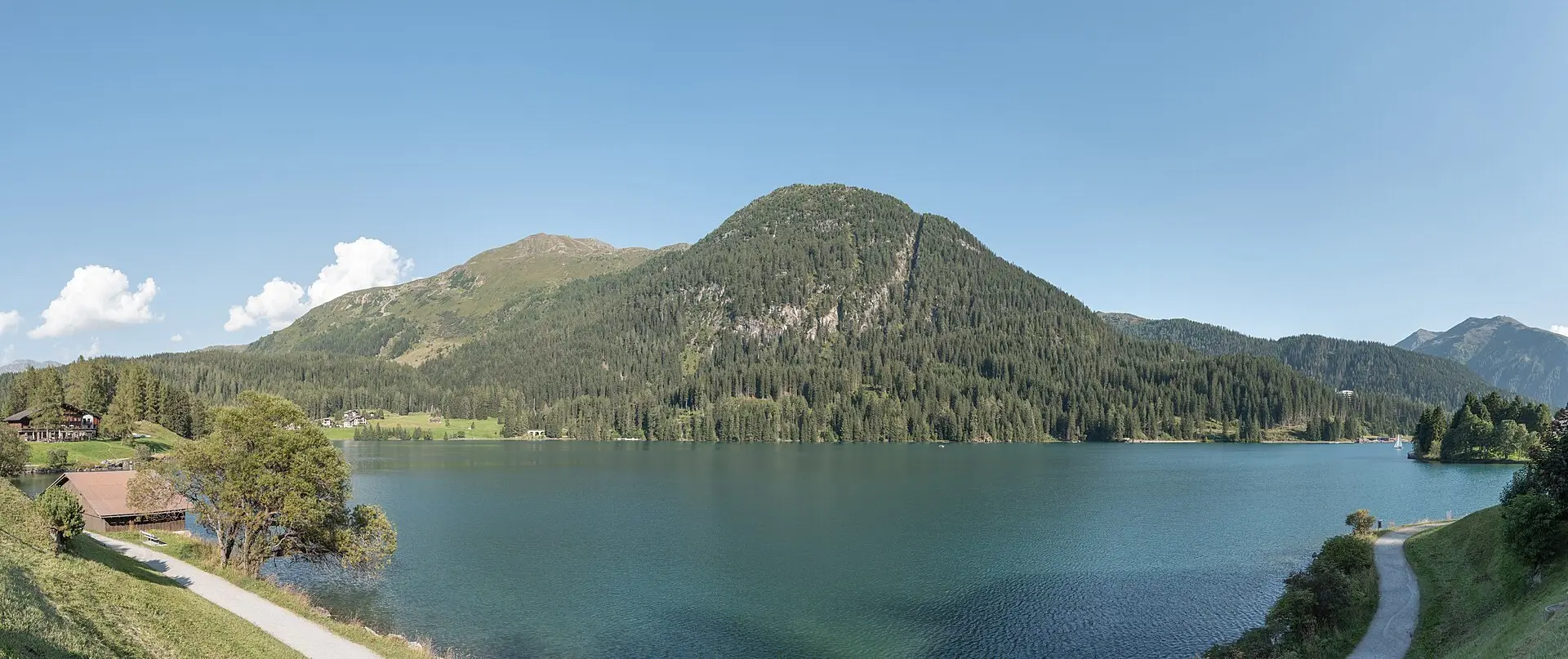 Family walking along the shore of Lake Davos with forested slopes and mountains behind