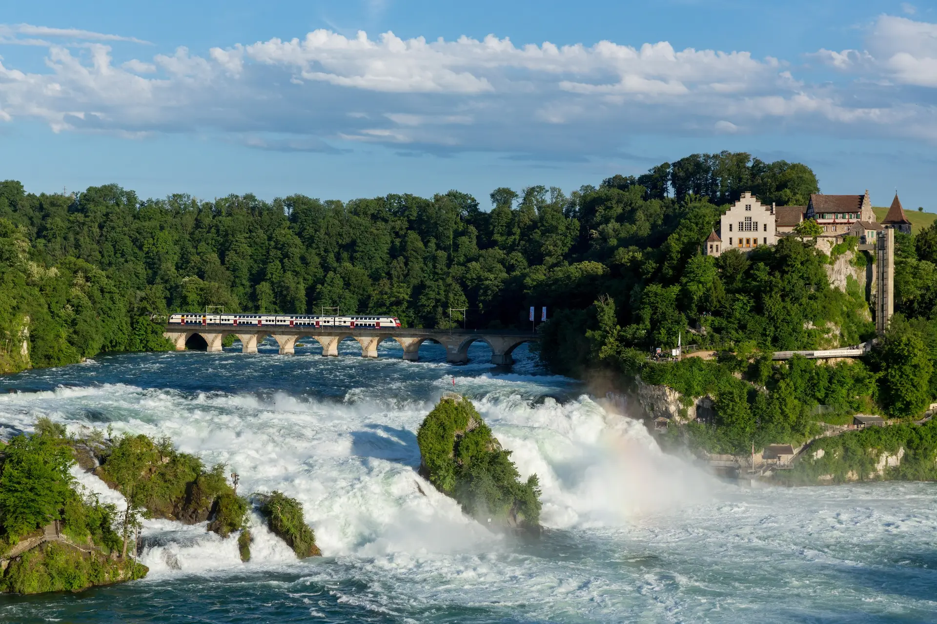 Couple on a viewing platform beside the Rhine Falls, spray and Schloss Laufen on the cliff above